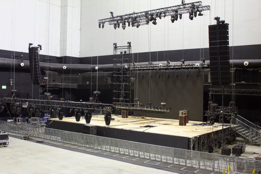 Installation of professional sound, light, video and stage equipment for a concert. Stage lighting equipment is clamped on a trusses for lifting. Line array sound speakers.